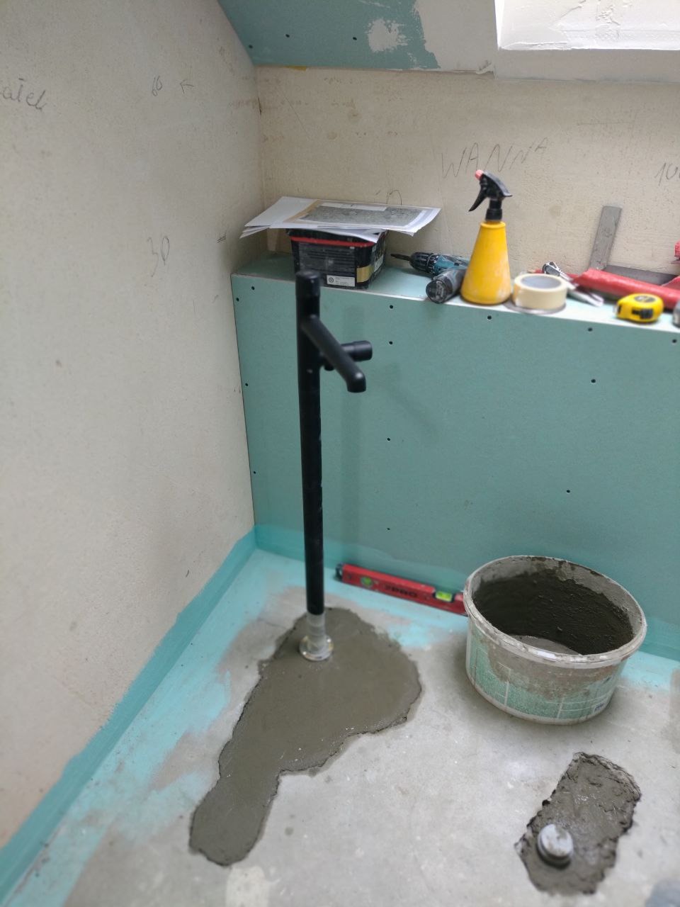 Montaż czarnej baterii umywalkowej w surowej łazience z widocznymi śladami prac wykończeniowych, świeżo wylana wylewka wokół podstawy, ściany przygotowane pod płytki, widoczne narzędzia i akcesoria...