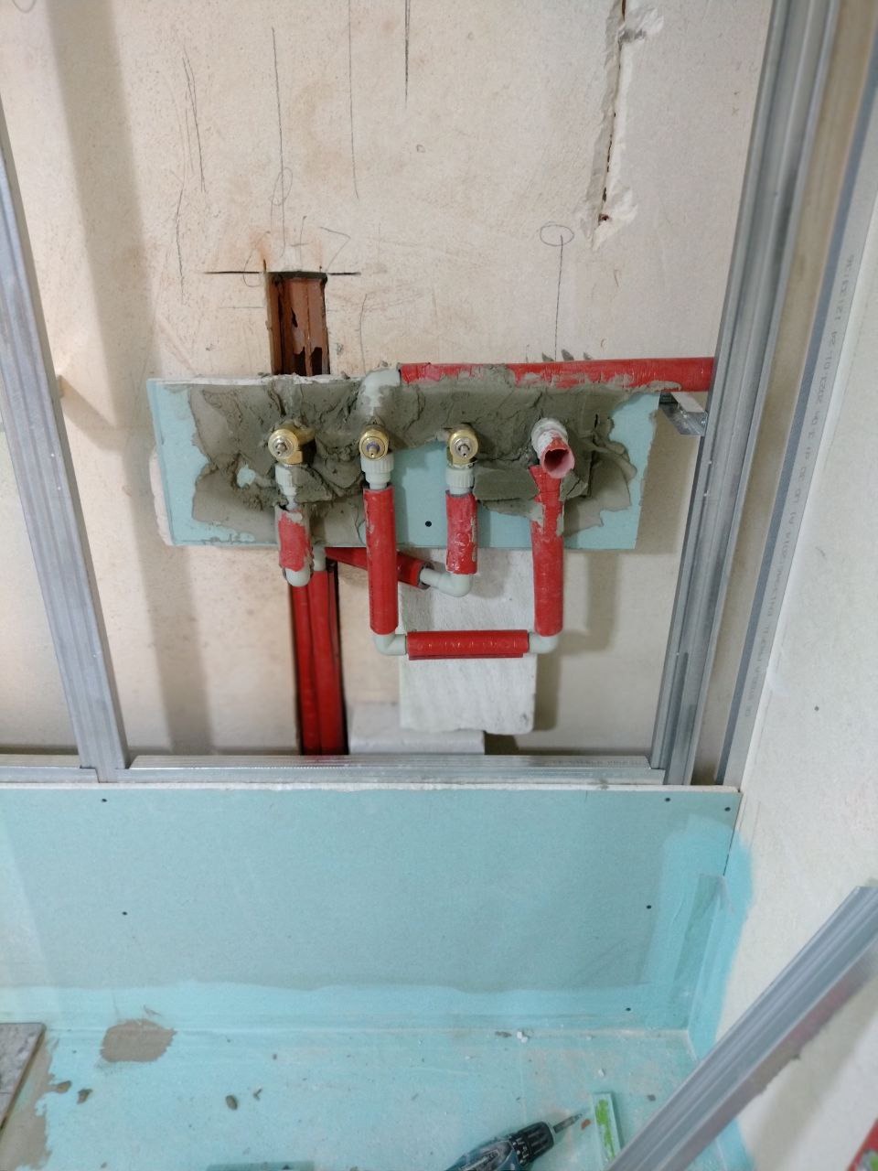 Przygotowanie instalacji wodnej z czerwonymi rurami w ścianie łazienki, widoczne profile montażowe i płyta gipsowo-kartonowa, etap prac przed położeniem płytek.