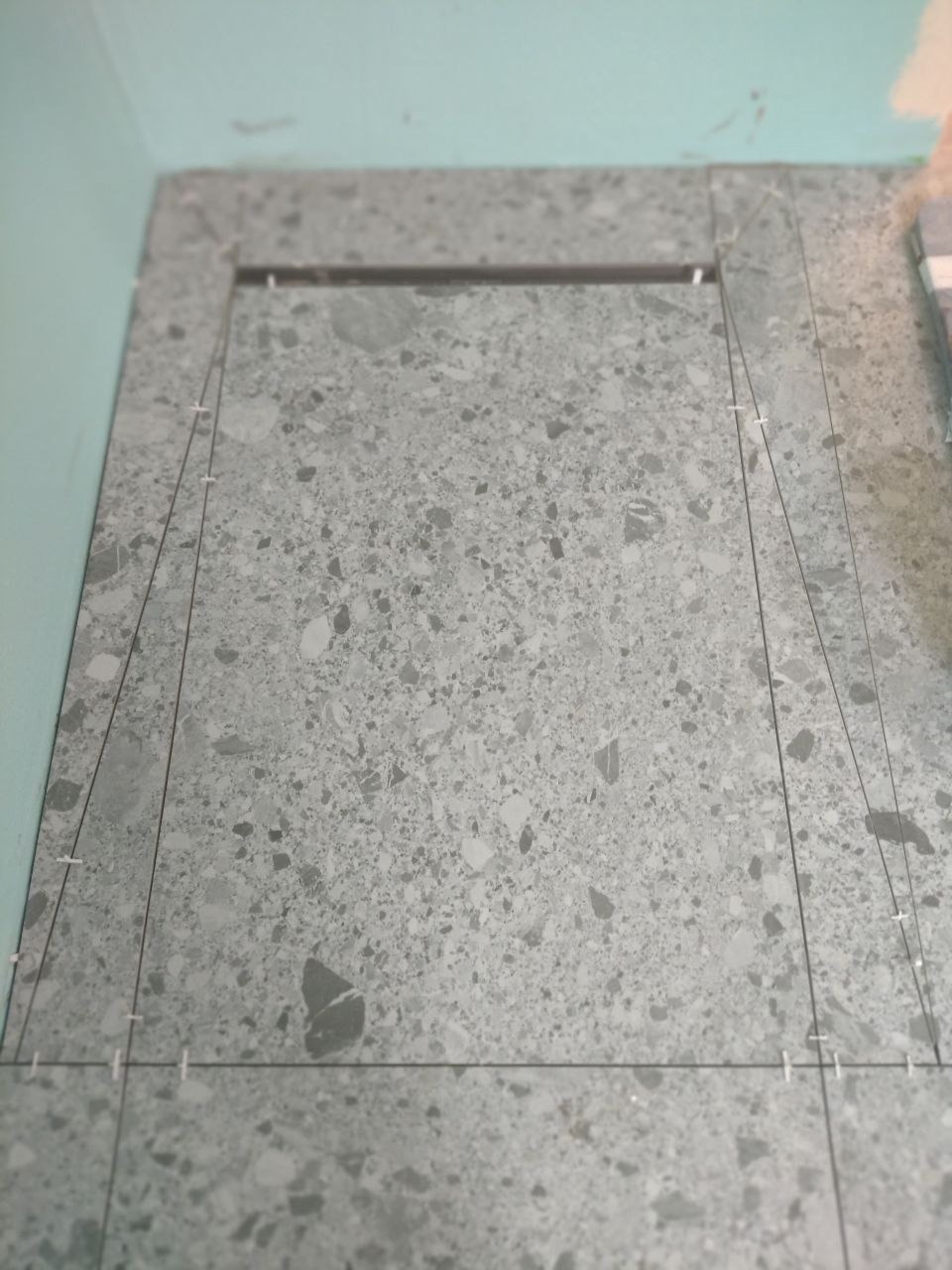 Układanie szarych płytek imitujących lastryko na podłodze z użyciem krzyżyków dystansowych i sznurka do wyznaczania linii.