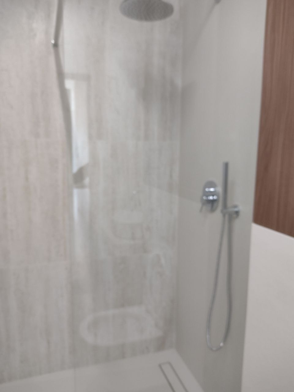 Nowoczesna kabina prysznicowa z deszczownicą, wykończona płytkami imitującymi marmur, widoczna armatura chromowana i odpływ liniowy.