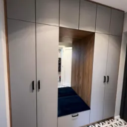 Szara szafa wnękowa z siedziskiem z granatową tapicerką, drewnianym wykończeniem i wzorzystą podłogą.