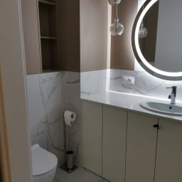 Meble wroclaw - Nowoczesna łazienka z toaletą, szafkami pod umywalką z białym blatem, okrągłym lustrem z podświetleniem LED i marmurowymi płytkami na ścianach.