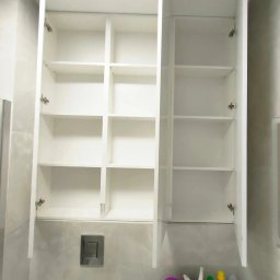 SN COMPANY SERHII NOVOMODNYI - Biała, otwarta szafka łazienkowa z półkami, zamontowana nad toaletą podwieszaną z widocznym przyciskiem spłukiwania. Na dole widoczne środki czystości.