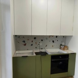 SN COMPANY SERHII NOVOMODNYI - Montaż kuchni: zielone szafki dolne z czarnym piekarnikiem, białe szafki górne, blat z wzorem lastryko, widoczne elementy instalacji elektrycznej.