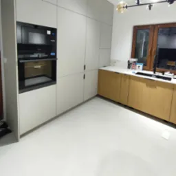 Nowoczesna kuchnia z zabudową w odcieniach szarości i drewna, z wbudowanym piekarnikiem i mikrofalówką, oświetlona lampą sufitową z kulistymi kloszami.