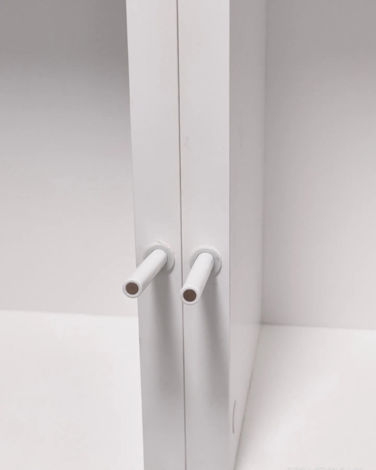 Białe drzwi szafy z dwoma uchwytami w kształcie krótkich rurek, widoczne wnętrze szafy w tle.