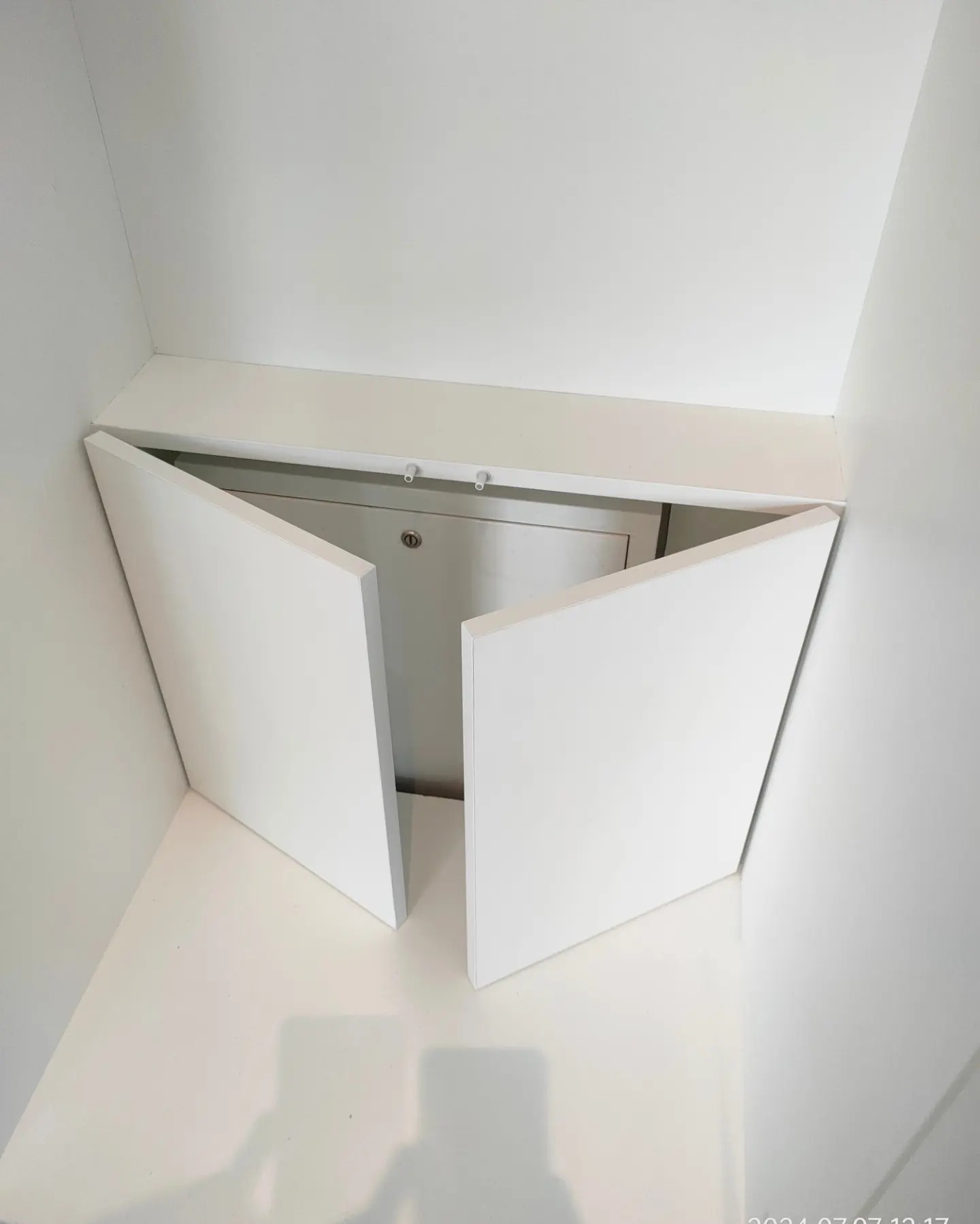 Biała szafka wnękowa z uchylonymi drzwiczkami, widok z dołu, minimalistyczny design.