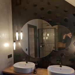 MajsterJan - Nowoczesna łazienka z dwoma umywalkami nablatowymi, czarnymi heksagonalnymi płytkami na ścianie i okrągłymi lustrami, w których odbija się osoba robiąca zdjęcie