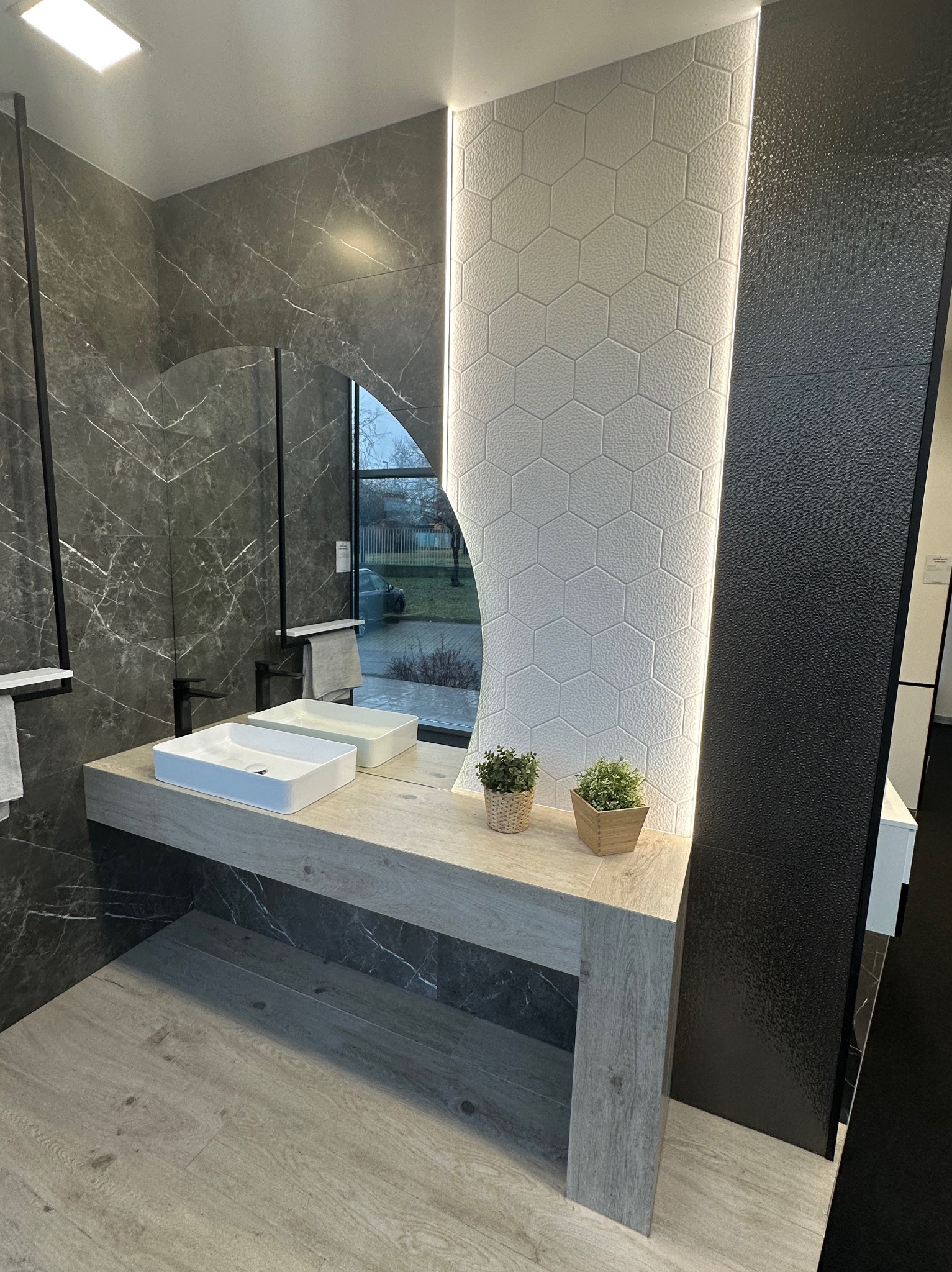 Nowoczesna łazienka z marmurowymi płytkami, umywalkami nablatowymi, lustrem z podświetleniem LED i dekoracyjnymi roślinami w doniczkach.