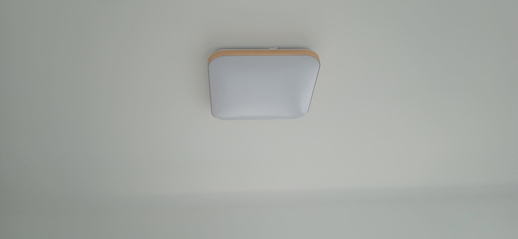 Kwadratowa lampa sufitowa LED z drewnianą ramką na białym suficie, widok z dołu.