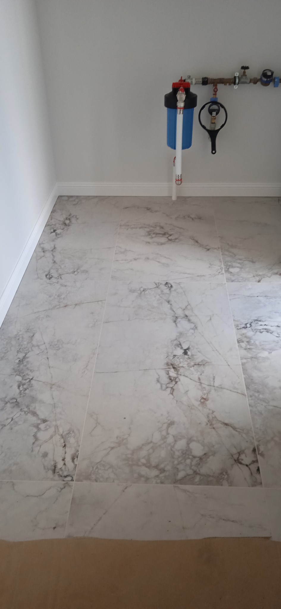 Podłoga wyłożona płytkami imitującymi marmur z widocznym filtrem do wody i instalacją wodną na ścianie.