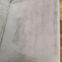 Szary, welurowy narożnik po praniu, widoczne jaśniejsze plamy po czyszczeniu na tle drewnianej podłogi.