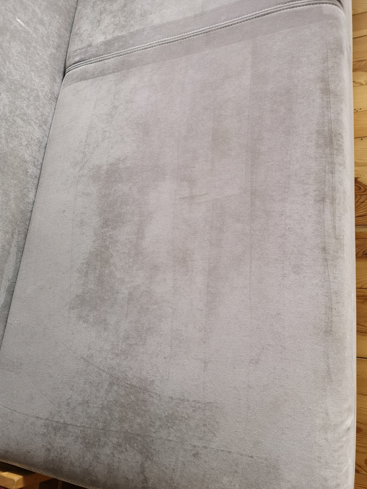 Szary, welurowy narożnik po praniu, widoczne jaśniejsze plamy po czyszczeniu na tle drewnianej podłogi.