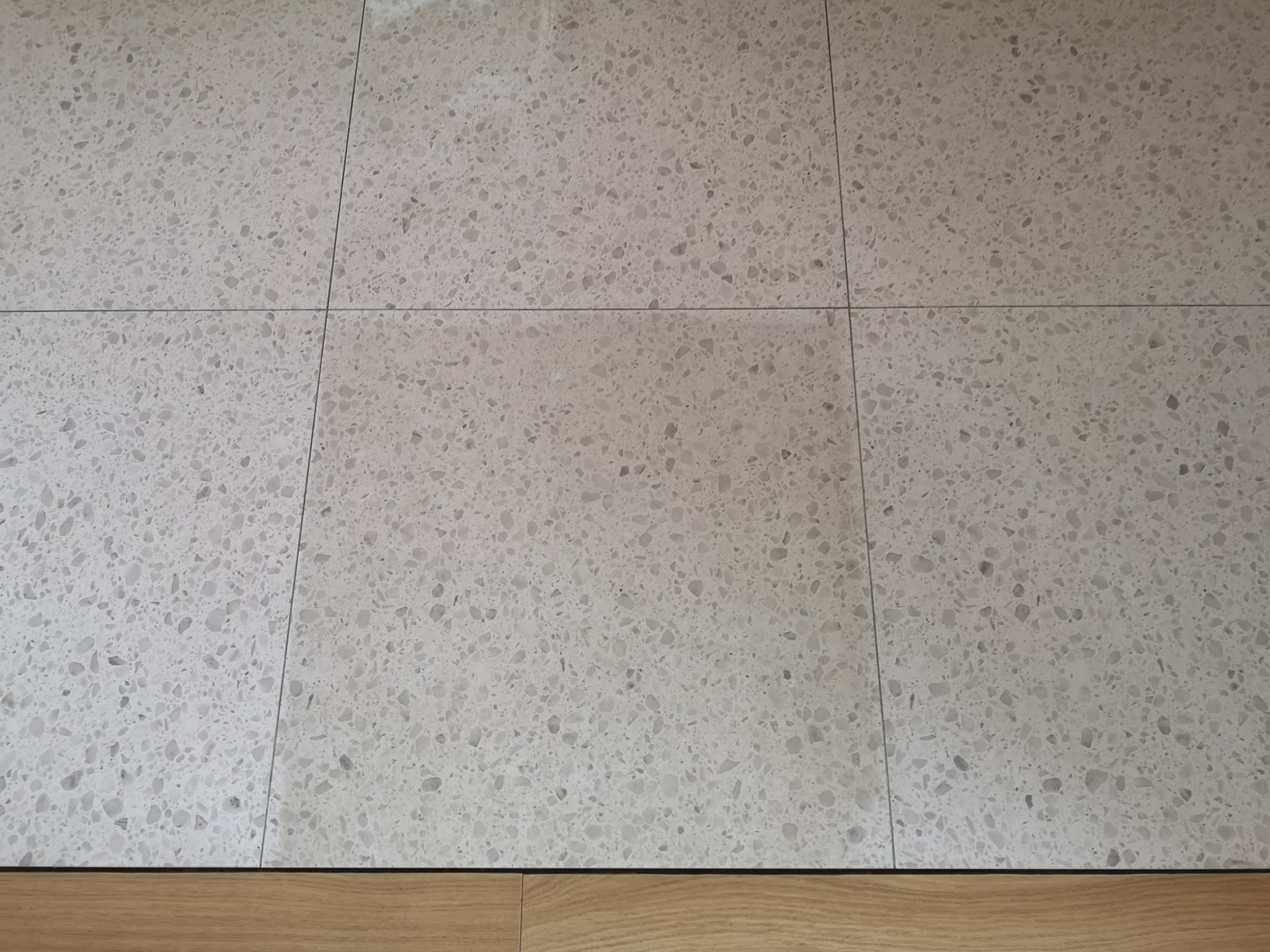 Jasnoszare płytki podłogowe z wzorem lastryko, ułożone na równej powierzchni, z widoczną drewnianą listwą przypodłogową