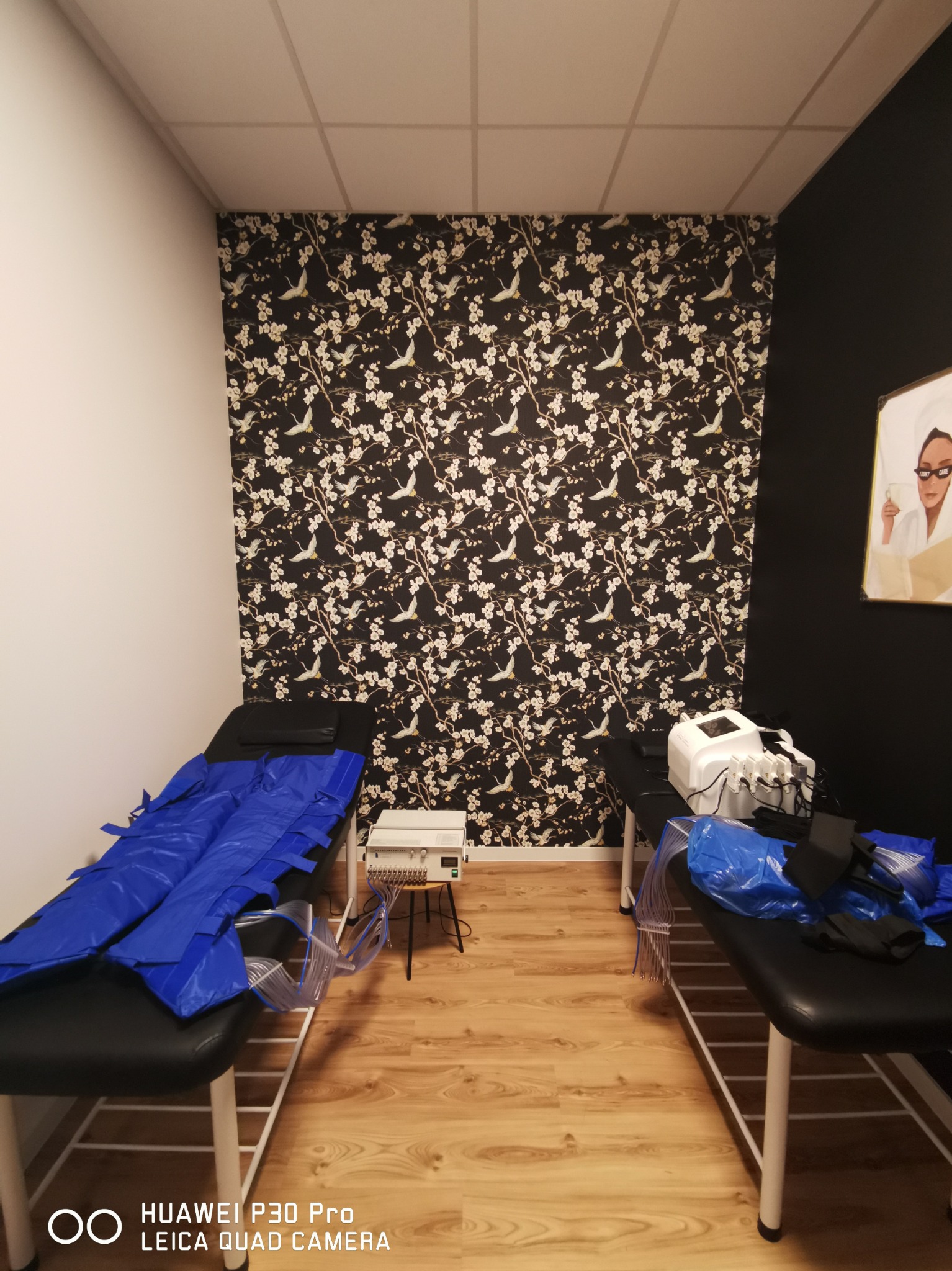 Pokój zabiegowy z dwoma leżankami do presoterapii, ściana w czarno-białe kwiaty i ptaki, jasna podłoga imitująca drewno.