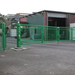 DEMEX SPÓŁKA Z OGRANICZONĄ ODPOWIEDZIALNOŚCIĄ - Zielona, metalowa brama przemysłowa z automatyką na tle budynku magazynowego z ceglaną elewacją i betonowym podjazdem.