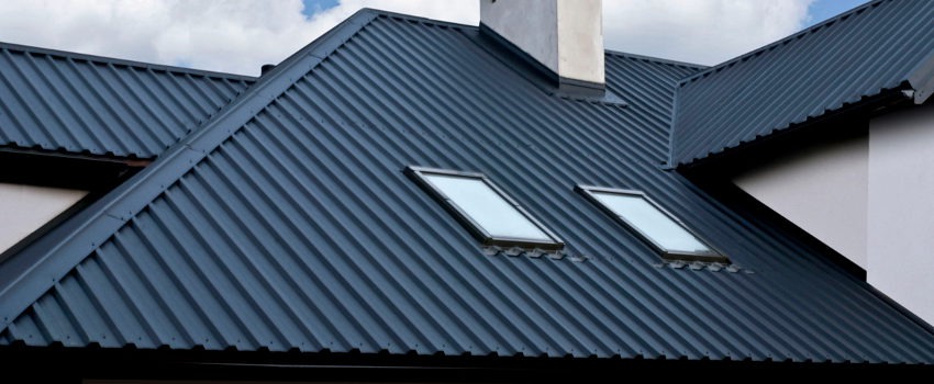 Nowoczesny dach z blachy na rąbek stojący w kolorze grafitowym z dwoma oknami dachowymi i kominem, widok z dołu.