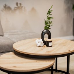 ZWOLMAR MEBLE NA WYMIAR - Zestaw dwóch okrągłych stolików kawowych z drewnianymi blatami i czarnymi metalowymi nogami, na większym stoliku czarny wazon z zielonymi gałązkami, biała dekoracja w kształcie węzła i czarna...