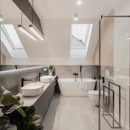 ZWOLMAR MEBLE NA WYMIAR - Nowoczesna łazienka na poddaszu ze skośnym sufitem i oknami dachowymi, wyposażona w dwie białe umywalki nablatowe, wolnostojącą wannę, szklaną kabinę prysznicową i grzejnik drabinkowy w kolorze...