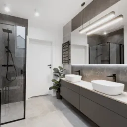 Nowoczesna łazienka z szarą armaturą, kabiną prysznicową z czarnymi ramami, dwiema białymi umywalkami na szarej szafce z drewnianym blatem, podświetlanym lustrem i grzejnikiem drabinkowym.