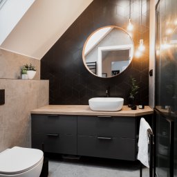 ZWOLMAR MEBLE NA WYMIAR - Nowoczesna łazienka na poddaszu z czarną ścianą z heksagonów, okrągłym lustrem, drewnianym blatem i szarą szafką pod umywalką oraz kabiną prysznicową ze szklanymi drzwiami.