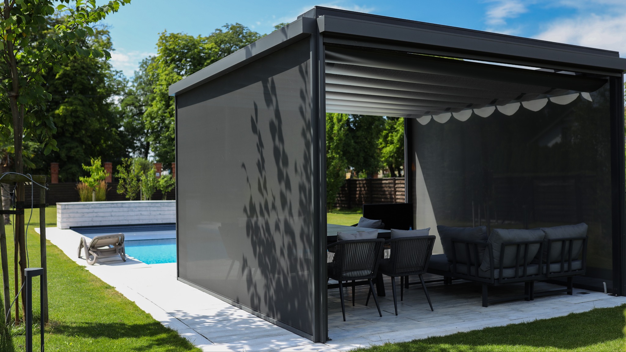 Nowoczesna pergola z rozsuwanymi panelami zacieniającymi, ustawiona obok basenu w ogrodzie.