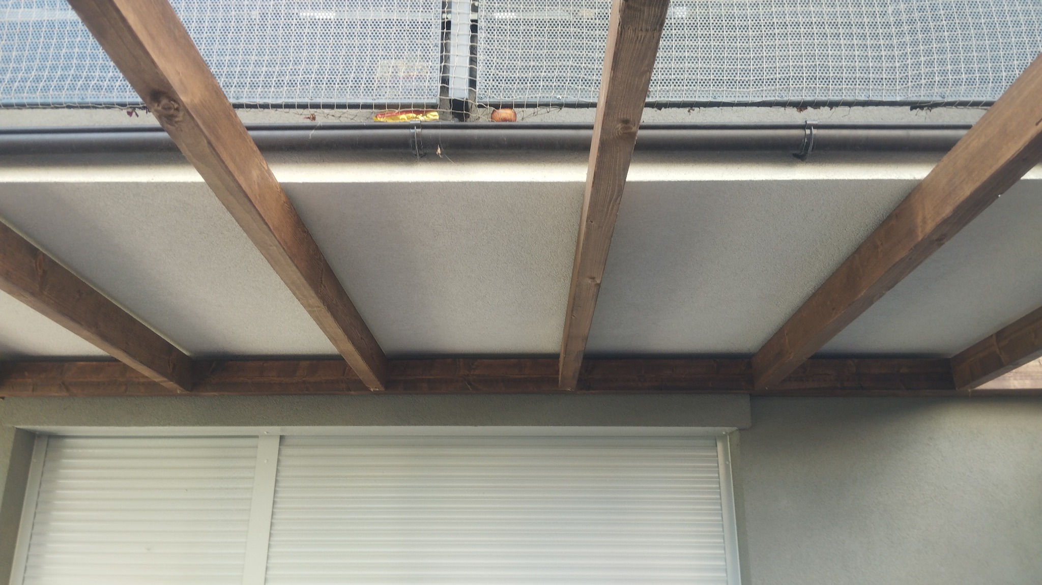 Widok z dołu na drewnianą konstrukcję zadaszenia z widocznymi tynkami i roletami zewnętrznymi
