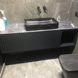 SoBo - Czarna umywalka nablatowa z marmurowym wzorem, zamontowana na szafce z ryflowanymi frontami w ciemnym kolorze, bateria ścienna, szara marmurowa ściana i podłoga.