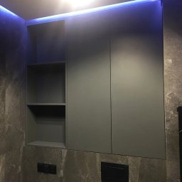 SoBo - Szara szafka łazienkowa z otwartą półką po lewej stronie, podświetlona od góry niebieskim światłem LED, na tle ściany wyłożonej płytkami imitującymi marmur.