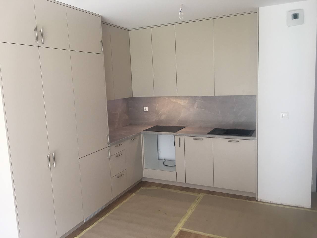 Jasna kuchnia z zabudową pod sufit i szarym blatem, widoczne przygotowane miejsce na sprzęt AGD, podłoga zabezpieczona folią malarską.