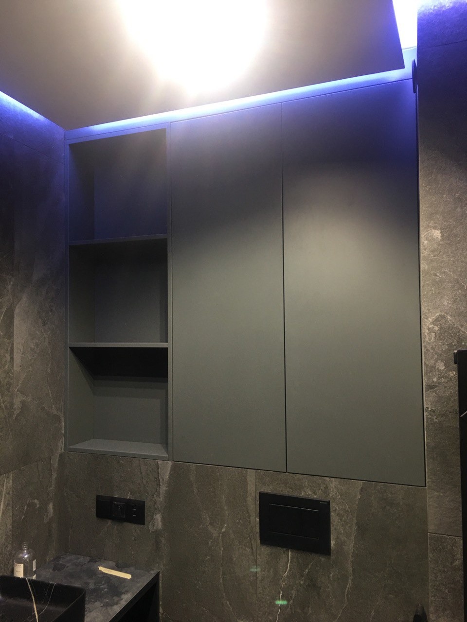 Szara szafka łazienkowa z otwartymi półkami i podświetleniem LED, zamontowana na ścianie z marmurowym wzorem.