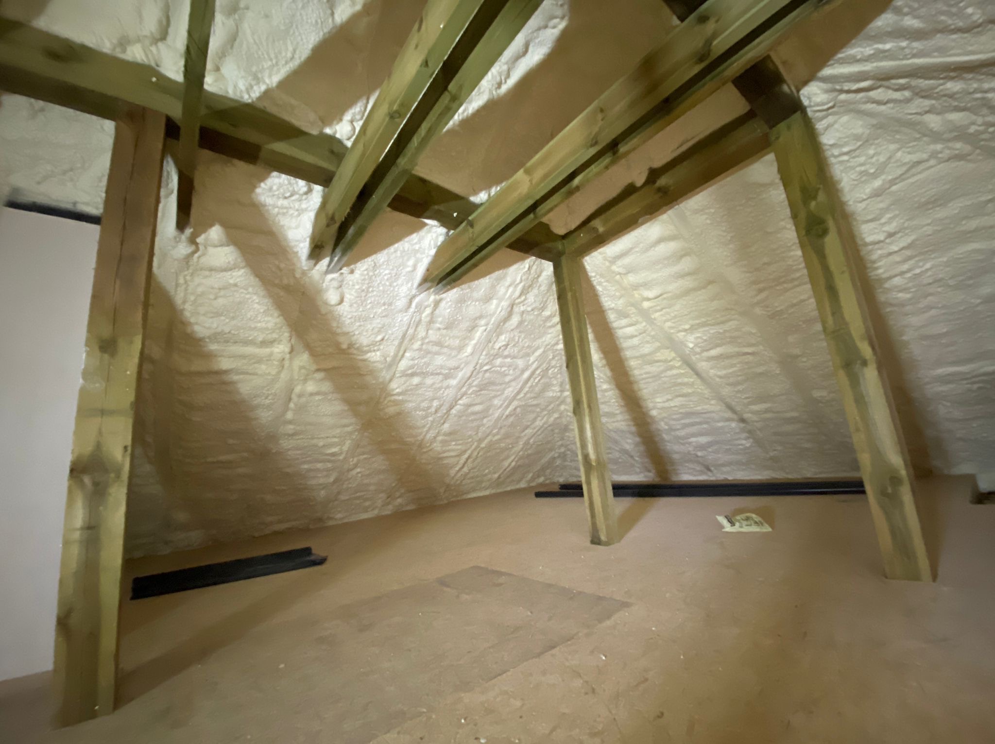 Poddasze po ociepleniu pianką PUR, widoczne drewniane krokwie i izolacja natryskowa na skośnych ścianach, fragment podłogi z widocznymi śladami po poprzedniej posadzce.