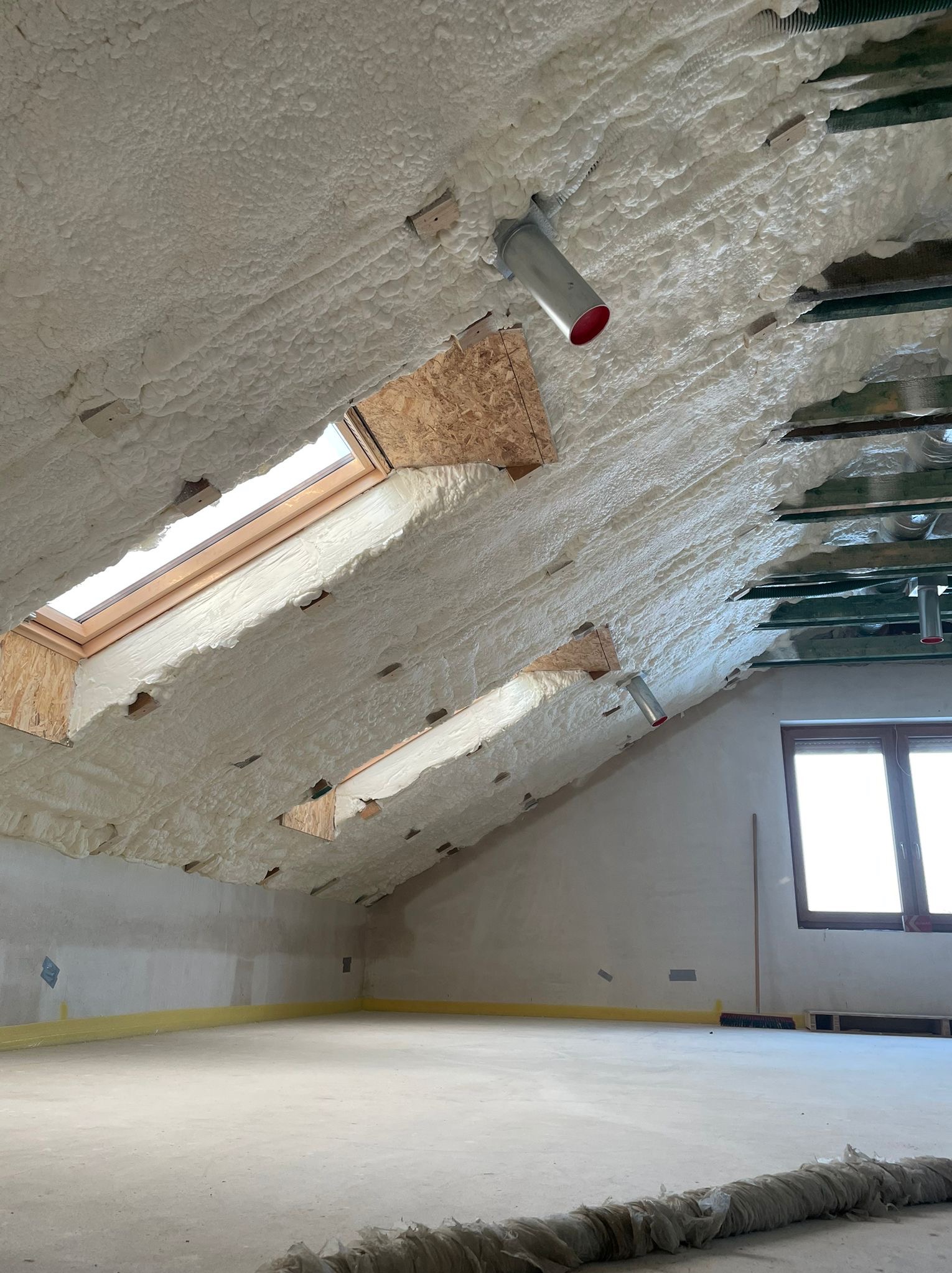 Poddasze po ociepleniu pianką PUR, widoczne okna dachowe, elementy konstrukcyjne i wentylacja, zabezpieczona żółtą folią dolna część ściany.