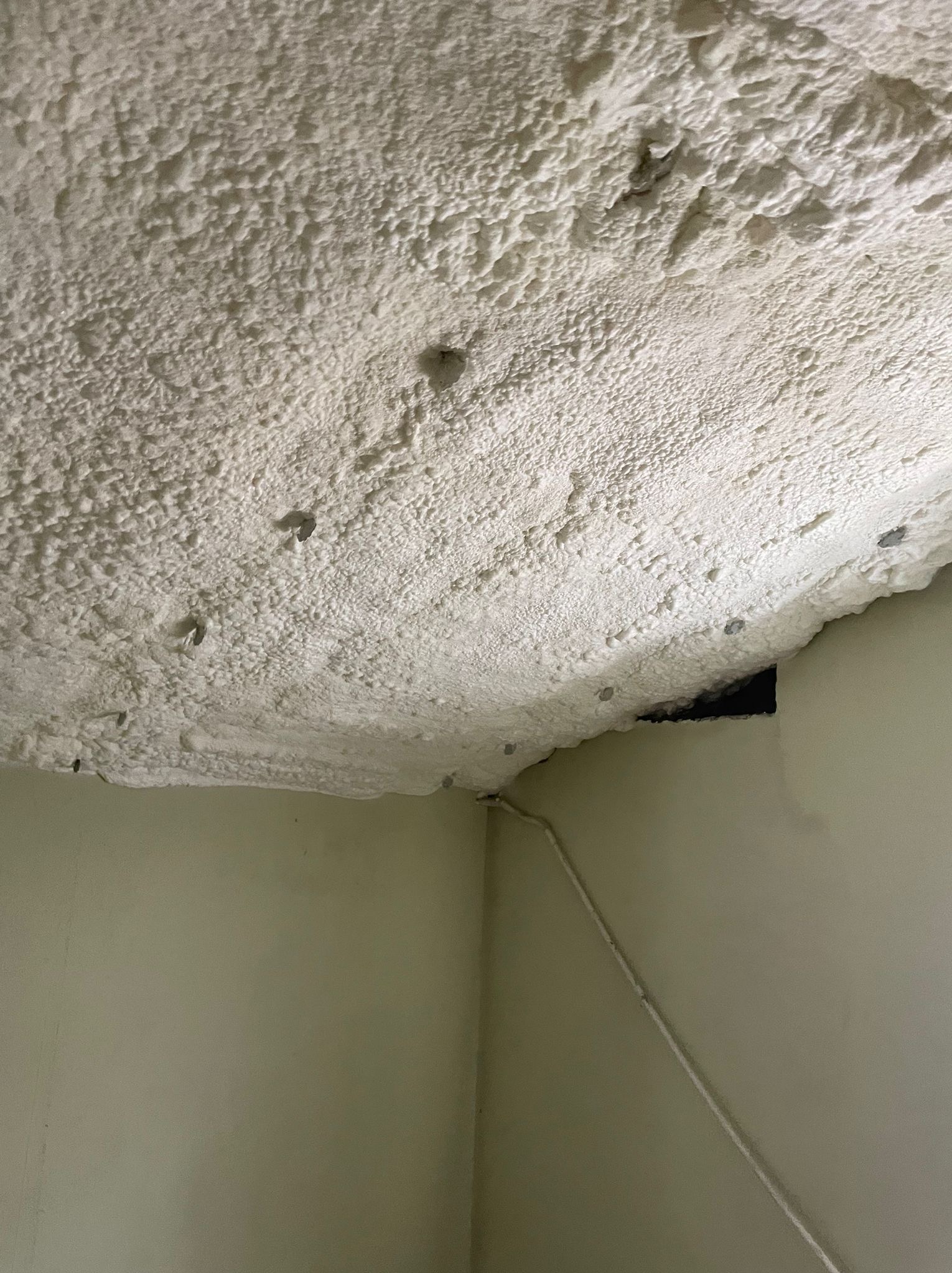 Poddasze po natrysku pianki izolacyjnej, widoczne nierówności struktury oraz fragment instalacji elektrycznej przy ścianie.