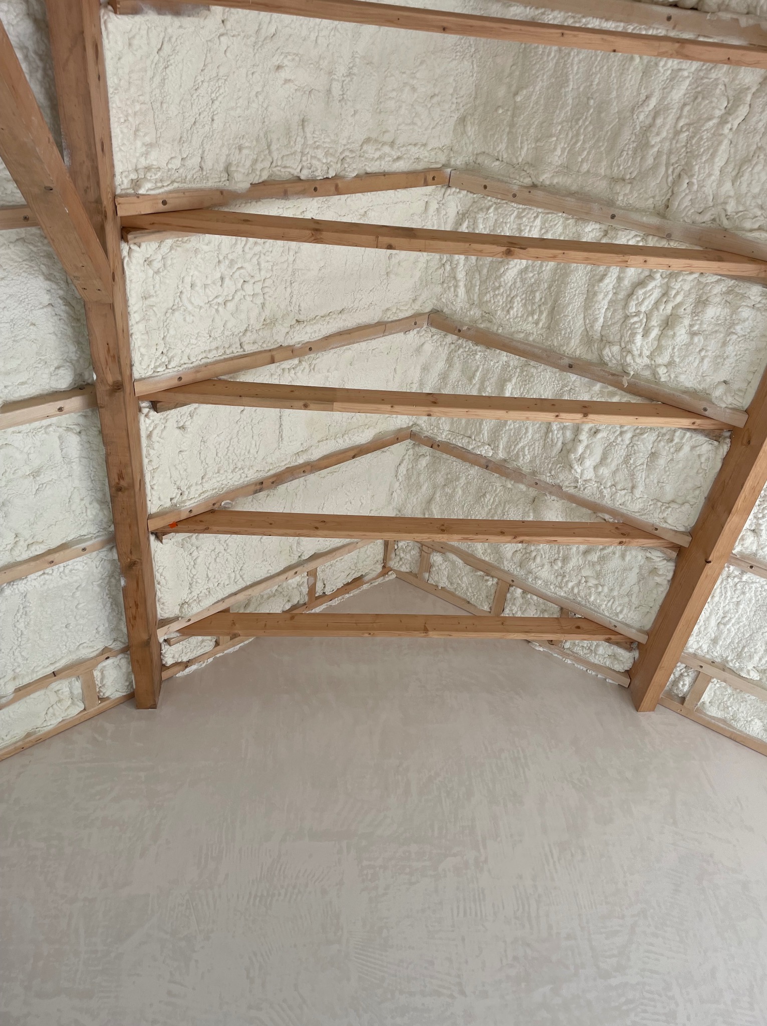 Poddasze z drewnianą konstrukcją krokwiową wypełnione białą pianką izolacyjną, widok od dołu.