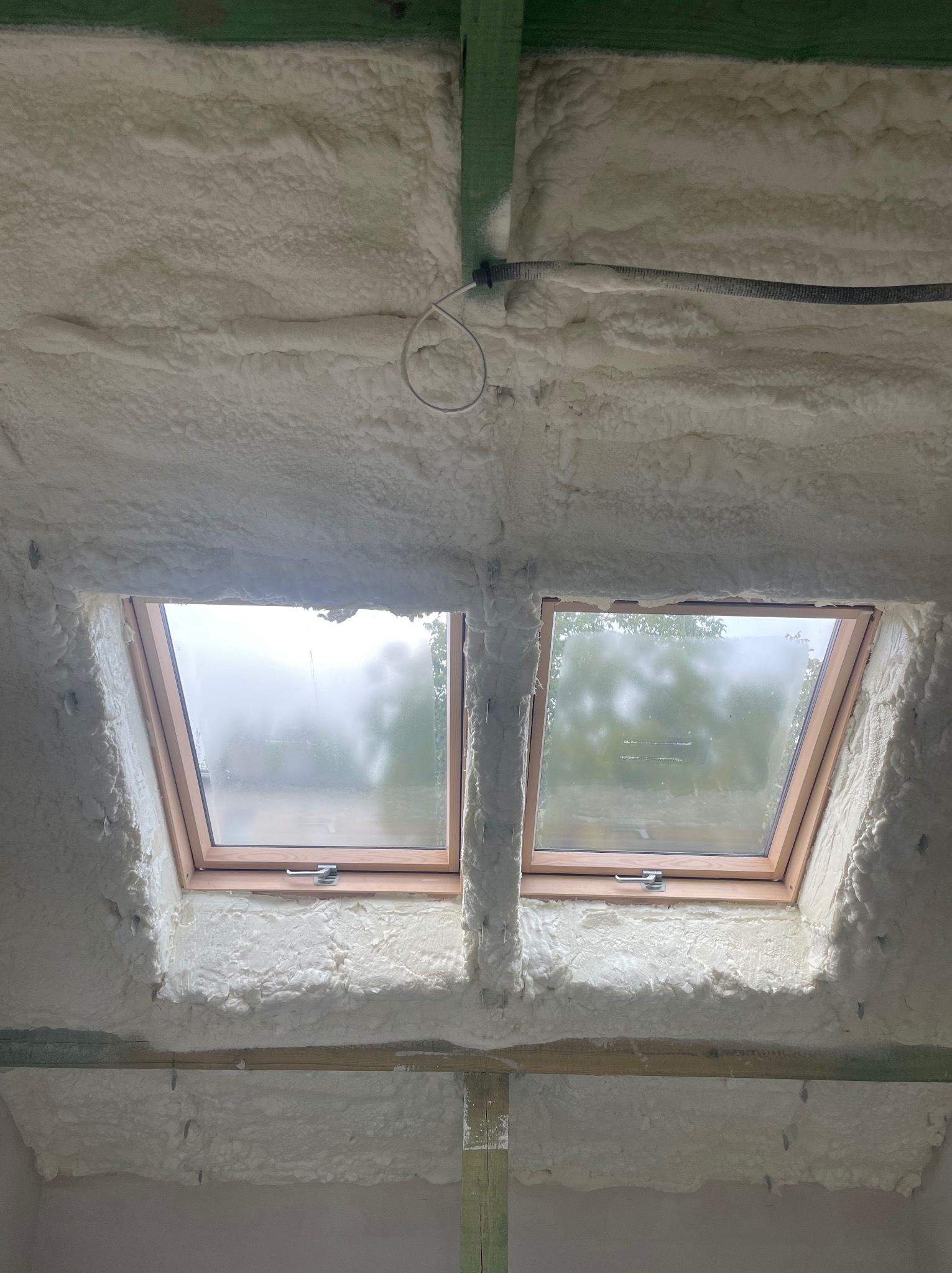 Poddasze z dwoma oknami dachowymi, ocieplone białą pianką PUR z widoczną strukturą i zielonymi elementami konstrukcyjnymi.