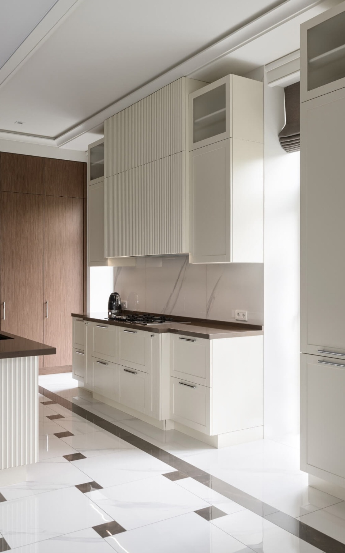 Elegancka, jasna kuchnia z białymi szafkami i ciemnym blatem, widok na płytki podłogowe z ciemnymi akcentami, zabudowa kuchenna z elementami ryflowanymi.