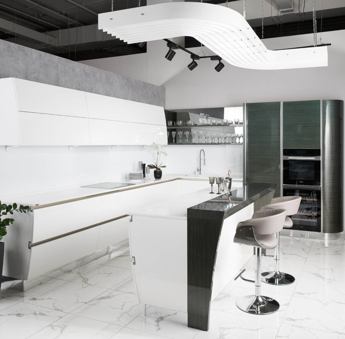 Nowoczesna kuchnia z białymi, lakierowanymi frontami, wyspą z barkiem i hokerami, oświetleniem punktowym i dekoracyjną lampą sufitową.