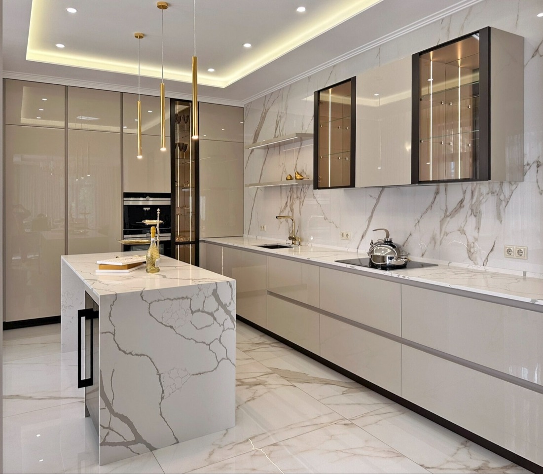 Luksusowa, jasna kuchnia z wyspą o marmurowym wzorze, błyszczące fronty szafek, złote detale oświetlenia i armatury, marmurowe ściany i podłoga.