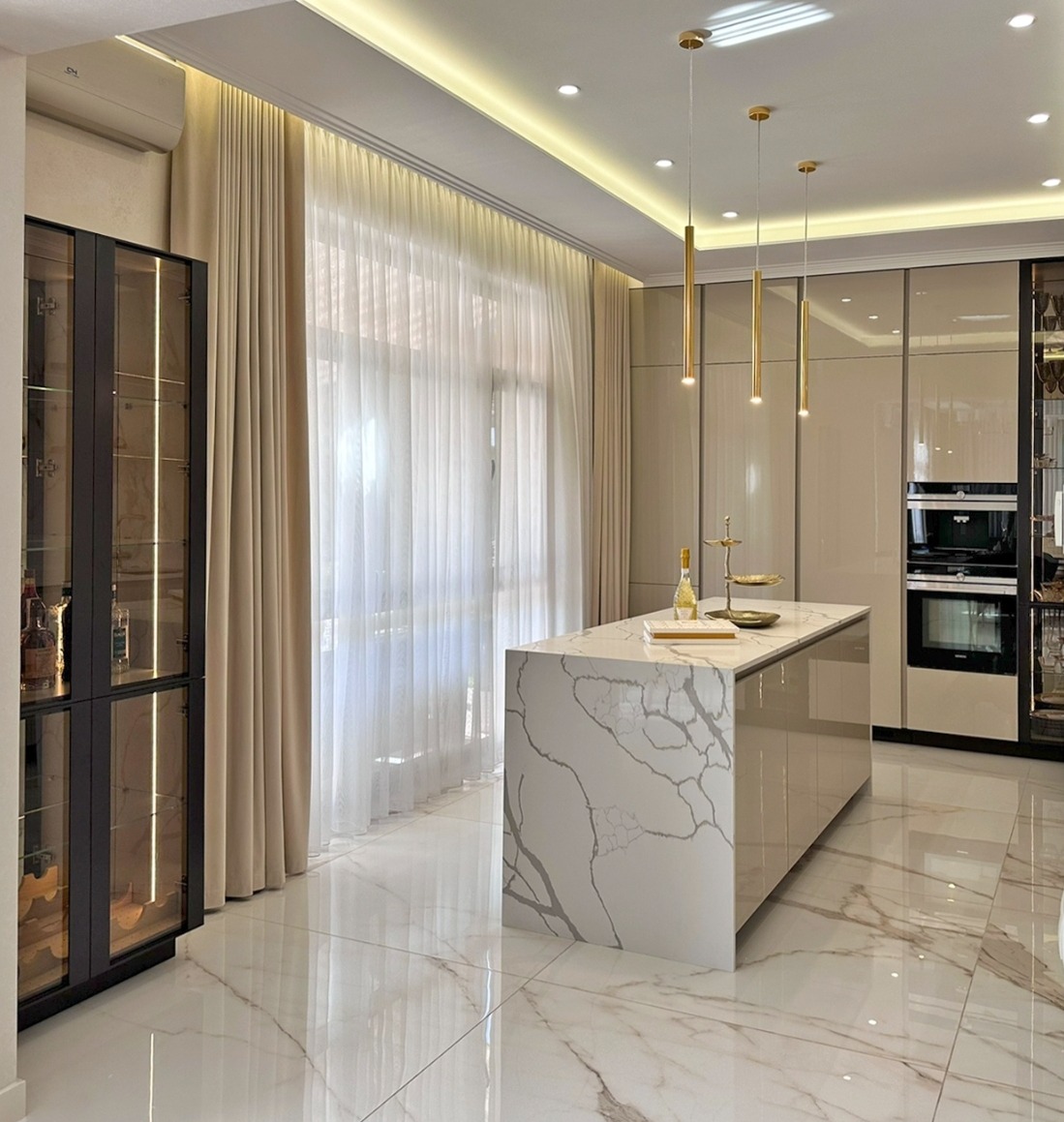 Elegancka kuchnia z wyspą o marmurowym wzorze, oświetlona złotymi lampami wiszącymi, z przeszkloną szafką i błyszczącą marmurową podłogą.