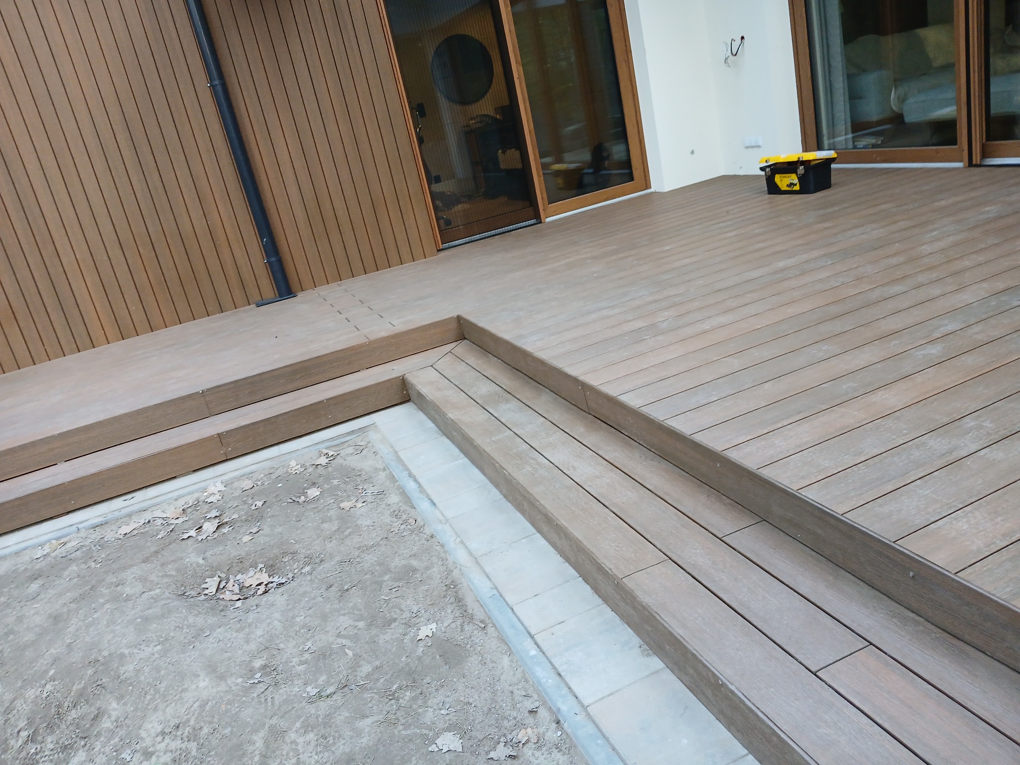 Montaż tarasu kompozytowego: deski ułożone schodkowo, widoczna skrzynka narzędziowa, częściowo wykończone obrzeże. Detal budowy tarasu.