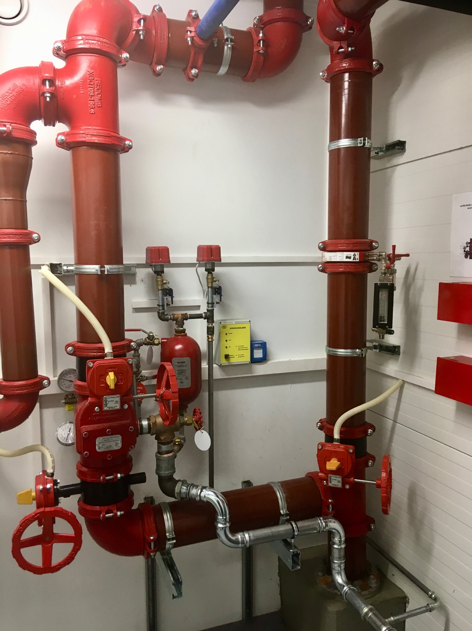 Rozbudowana instalacja rurociągowa w kolorze czerwonym i brązowym, z licznymi zaworami, manometrami i elementami mocującymi, z widocznymi rurami ze stali nierdzewnej u dołu, zamontowana...