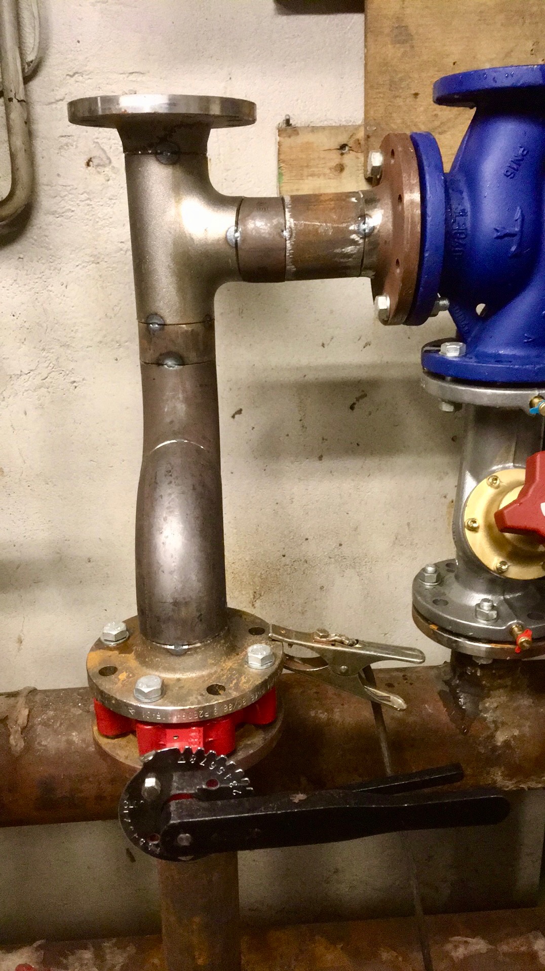 Spojenie rur stalowych z kołnierzami, widoczne spawy, zacisk ślusarski i klucz nastawny na tle ściany.