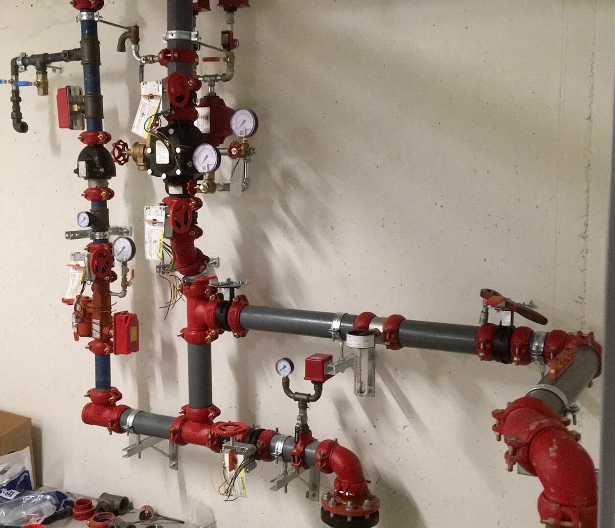 Kompleksowy system rur, zaworów i manometrów, pomalowanych na czerwono i szaro, zamontowany na ścianie w Skokach. Widoczne przewody elektryczne i elementy montażowe.