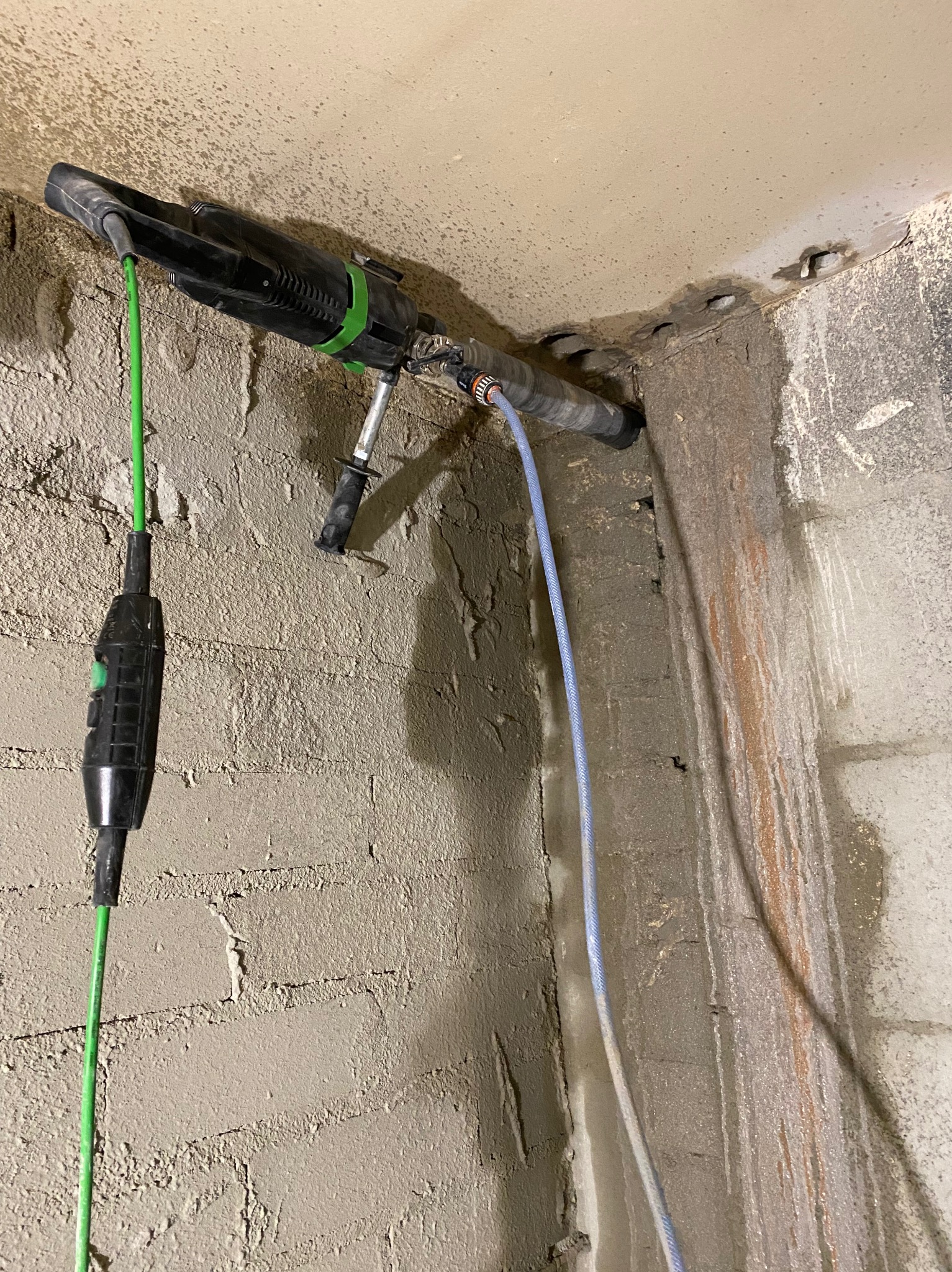 Wiertnica diamentowa przymocowana do ściany podczas wiercenia otworów pod instalację; widoczne przewody i ślady wiercenia.