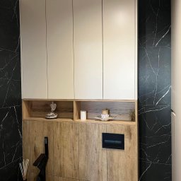 MG Meble na wymiar - Nowoczesna łazienka z białymi szafkami wiszącymi, drewnianą zabudową, czarnym marmurem na ścianach i minimalistyczną armaturą.