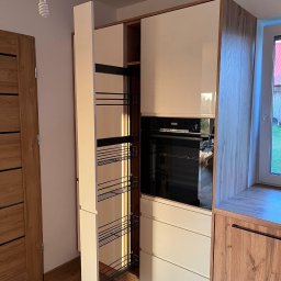 MG Meble na wymiar - Nowoczesna zabudowa kuchenna z otwartym, wysuwanym systemem cargo, jasnymi frontami i wykończeniem w kolorze drewna, z widocznym piekarnikiem w zabudowie.