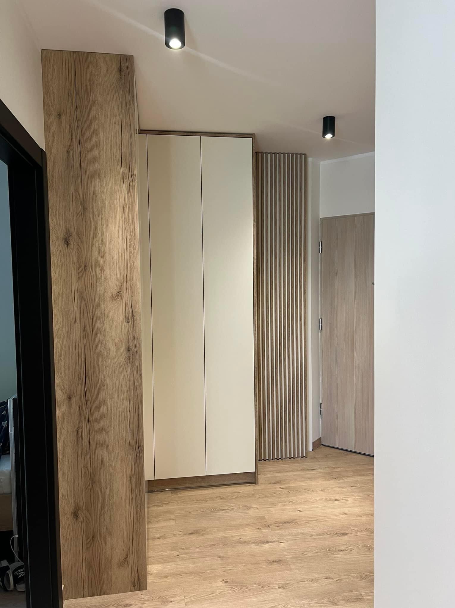 Nowoczesna szafa w przedpokoju z drewnianymi akcentami i oświetleniem punktowym.