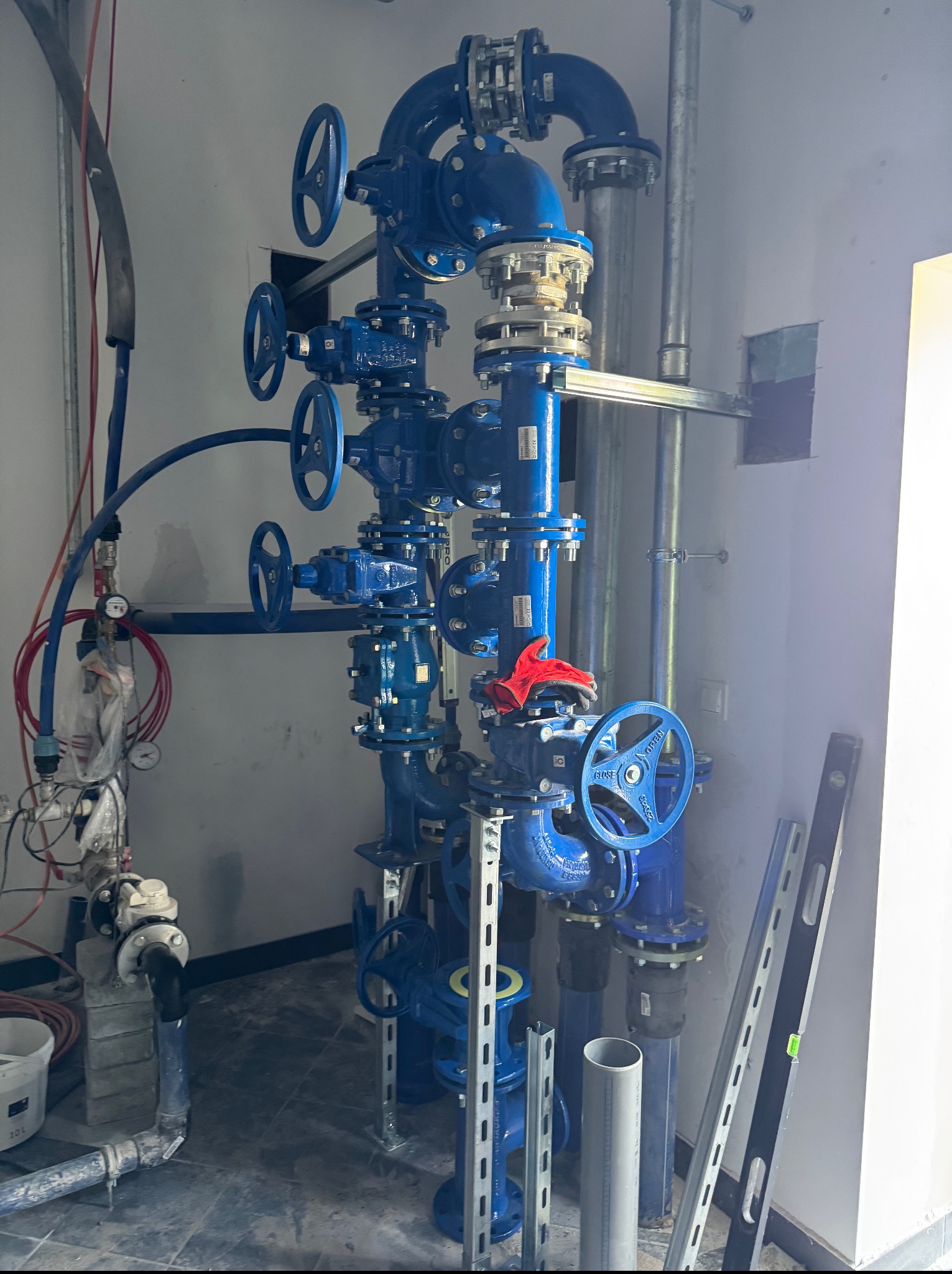 Niebieska instalacja wodna z zaworami motylkowymi i poziomnicami, w pomieszczeniu technicznym. Elementy instalacji są nowe i czyste, co sugeruje świeży montaż.