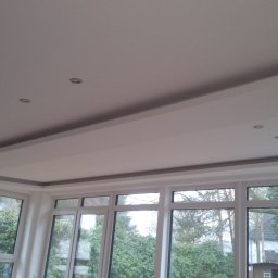 PIMMAR SPÓŁKA Z OGRANICZONĄ ODPOWIEDZIALNOŚCIĄ - Nowoczesny sufit podwieszany z oświetleniem punktowym w nowym domu z dużymi oknami wychodzącymi na ogród.